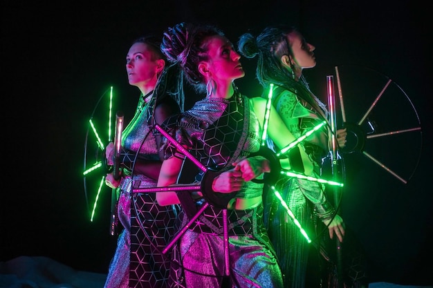 Drie mooie vrouwen in futuristische kostuums op een donkere achtergrond.