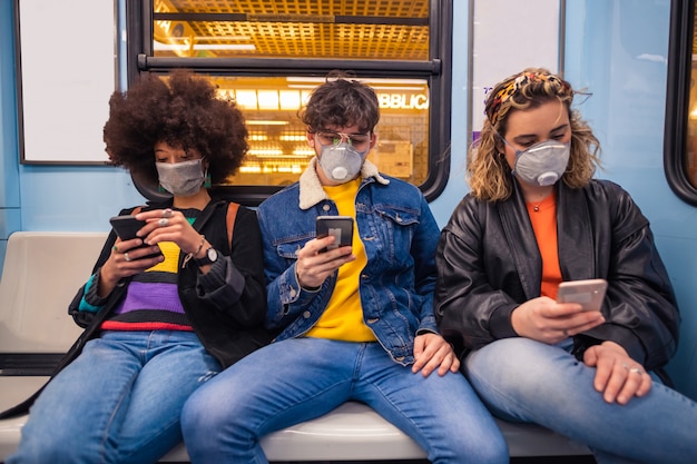 Drie multi-etnische vrienden dragen medische masker beschermen tegen vervuiling en virussen in de metro met smartphone