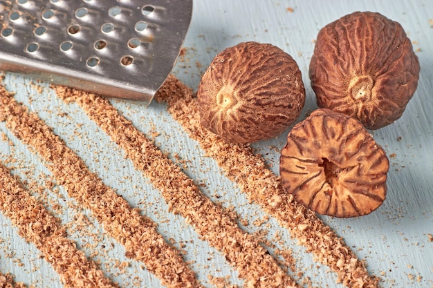 Drie muskaatnoten een metalen grater en sporen van muskaatnootpoeder op een houten tafel