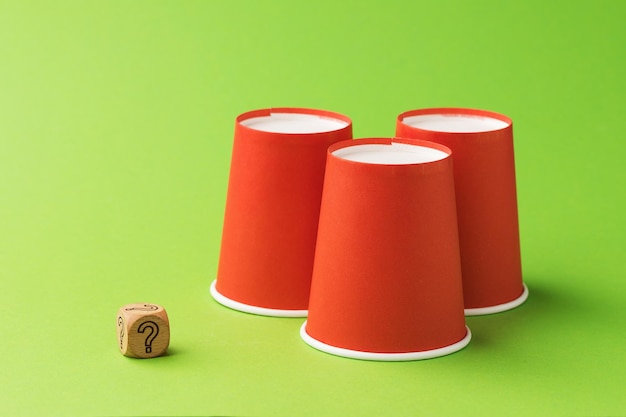 Drie oranje papieren bekers en een houten kubus met een vraagteken