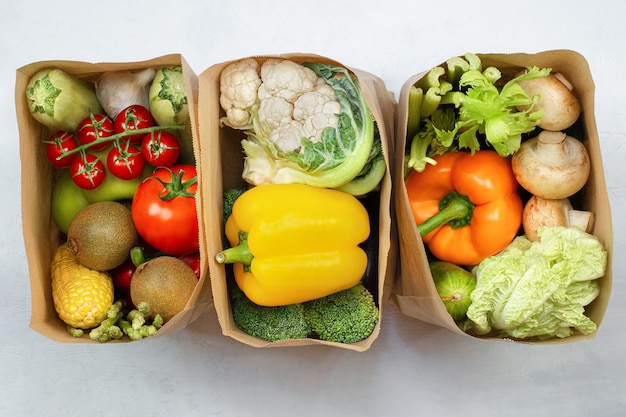 Drie papieren zakken met verse groenten en fruit op een lichttafel, bovenaanzicht