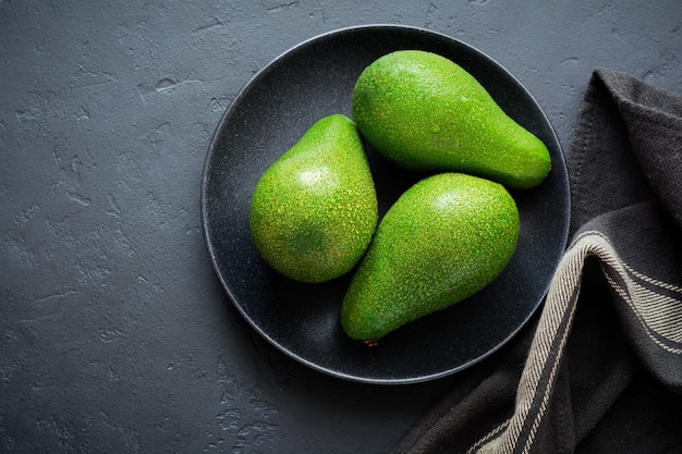 Drie rauwe verse avocado's in zwarte ceramische plaat