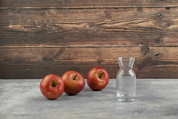Drie rode appels en leeg glas op marmeren oppervlak.