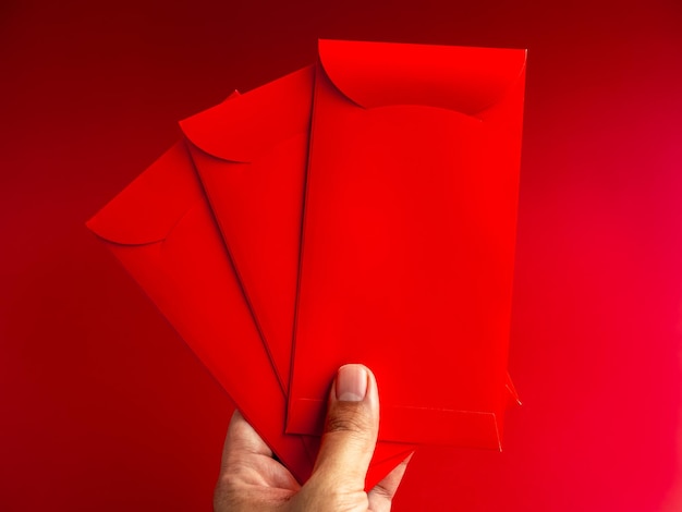 Foto drie rode enveloppen met de hand geïsoleerd op rode achtergrond 3 hongbao-pakketten voor geluksgeldgeschenk in chinees nieuw maanjaar op januari-maand bruiloft rood pakket