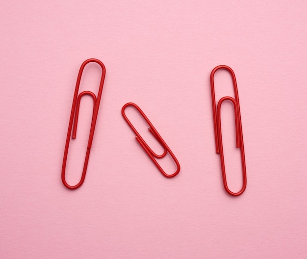 Drie rode metalen paperclips op een roze ruimte