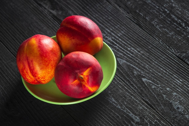 Drie rode rijpe nectarine-hybriden liggen in hun rijpingsseizoen op een groene plaat of donkere vintage tafel