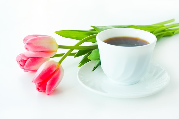 Drie roze tulpen en een kopje koffie op een witte tafel.