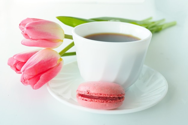 Drie roze tulpen, macarons en een kopje koffie op een witte tafel.