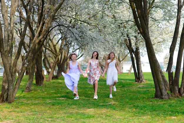 Drie schattige meisjes in jurken houden handen in een cirkel, hand in hand. Lente, tuin.