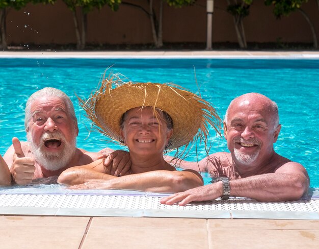 Drie senior gelukkige mensen die plezier hebben in het zwembad onder de zon - twee broers, gezichtsuitdrukking, glimlach en lach