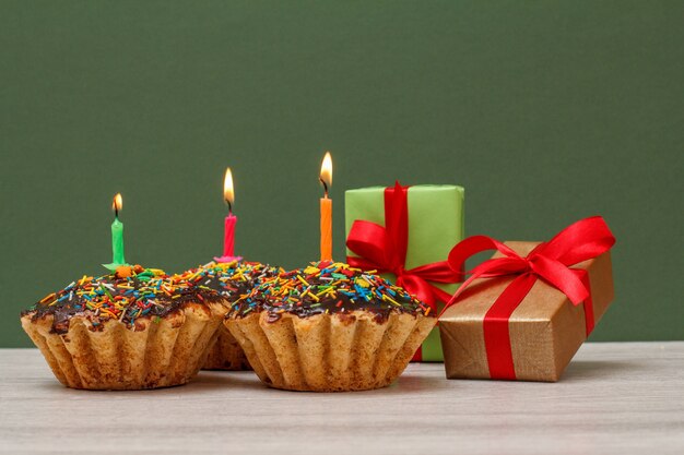 Drie smakelijke verjaardagscupcakes met chocoladeglazuur en karamel, versierd met brandende feestelijke kaarsen en geschenkdozen op groene achtergrond. gelukkige verjaardag minimaal concept.