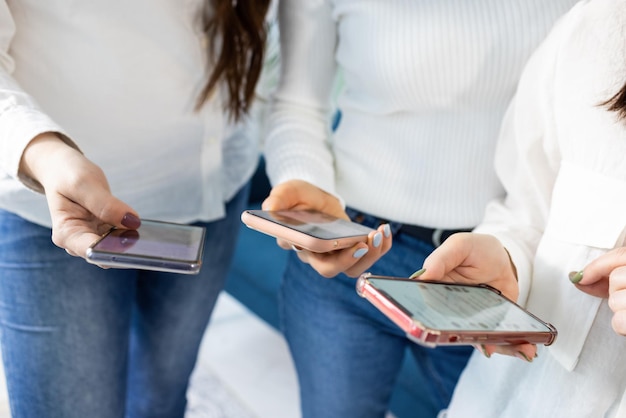 Drie smartphones in de handen van meisjes in shirts en jeans in de studio