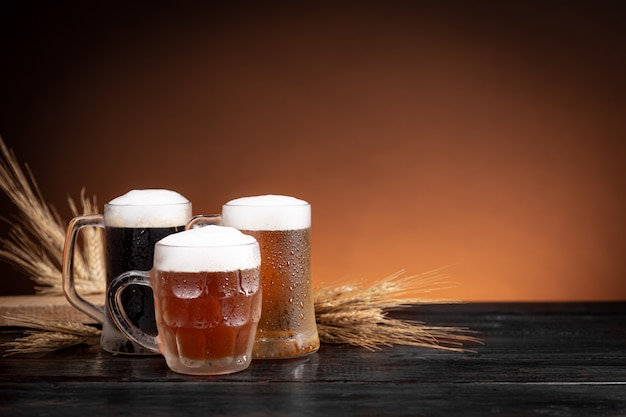 Drie soorten koud bier in kannen en tarwespikes op houten basis.