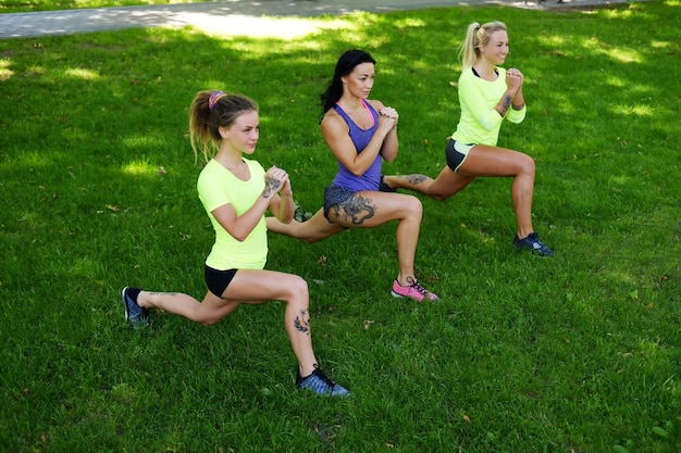 Drie sportieve vrouwtjes opwarmen op een grasveld in het zomerpark.