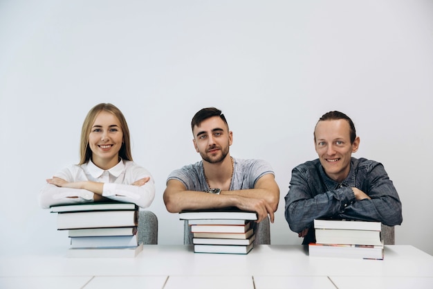 Drie studenten zitten aan de tafel met boeken in witte kamer