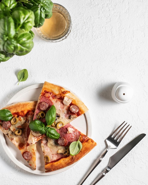 Drie stukken pizza in witte plaat mes en vork en basilicum bladeren op witte tafel Bovenaanzicht