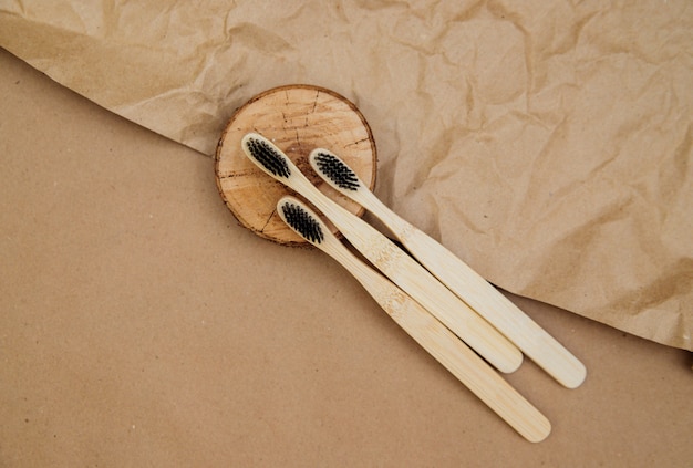 Foto drie tandenborstels van natuurlijk bamboe liggen op een stuk hout, tegen een achtergrond van bruin kraftpapier. een duurzame levensstijl en een plasticvrij concept, badkamer essentials.