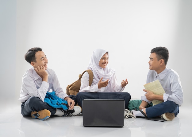 Drie tieners in junior high school uniformen zittend op de vloer samen studeren en kletsen met...