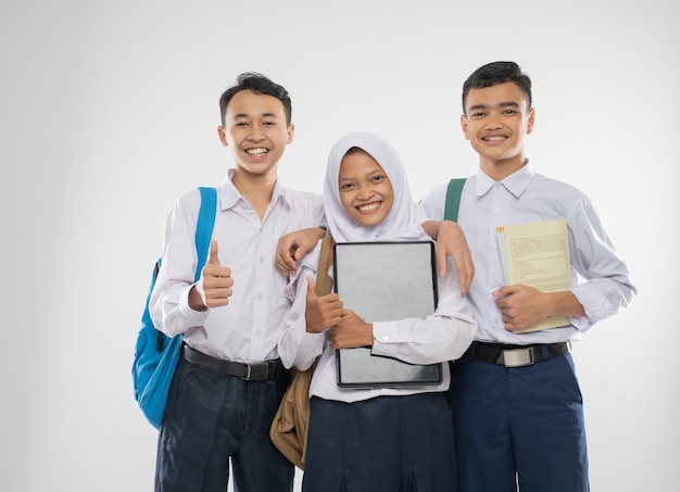 Drie tieners in middelbare schooluniformen houden een laptop vast met hun duimen omhoog tijdens het dragen...