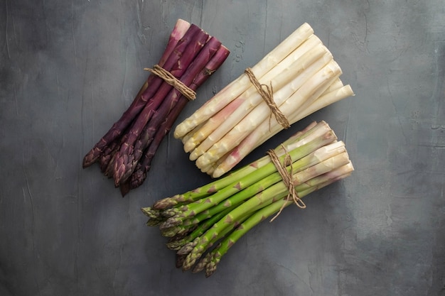 Drie trossen van verschillende verse asperges geïsoleerd op grijs. Paars witte en groene asperges. Verse groenten.