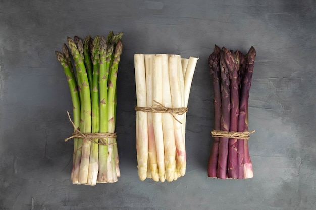 Drie trossen van verschillende verse asperges geïsoleerd op grijs. Paars witte en groene asperges. Verse groenten.