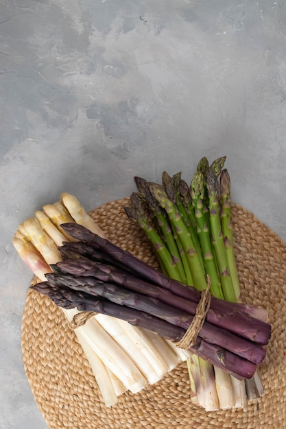 Drie trossen van verschillende verse asperges geïsoleerd op grijs. Paars witte en groene asperges. Verse groenten.