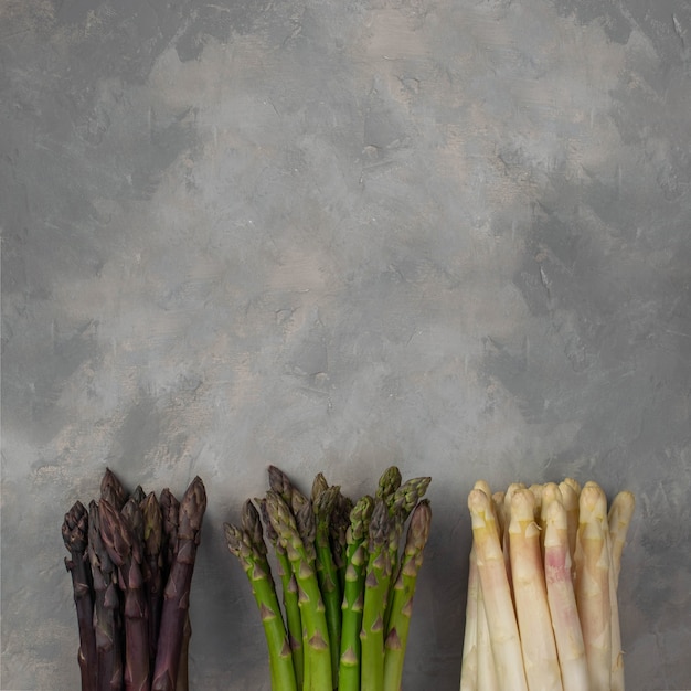 Drie trossen van verschillende verse asperges geïsoleerd op grijs. Paars witte en groene asperges. Verse groenten.