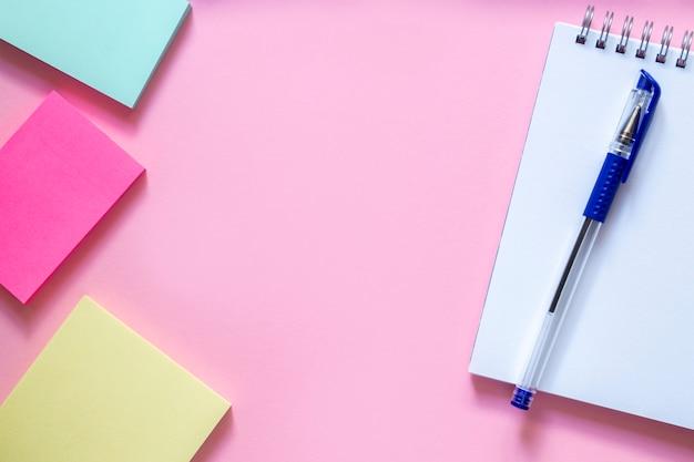 Drie veelkleurige stickers op een delicate roze tafel, een wit notitieboekje met een spiraal en een blauwe pen