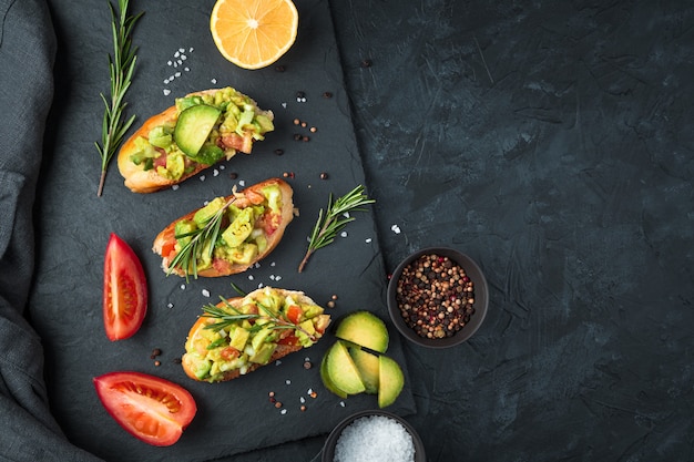 Drie verse guacamole sandwiches en tomaten op een platte schotel op een zwarte betonnen tafel. Bovenaanzicht, met ruimte om te kopiëren. Het concept van goede voeding.