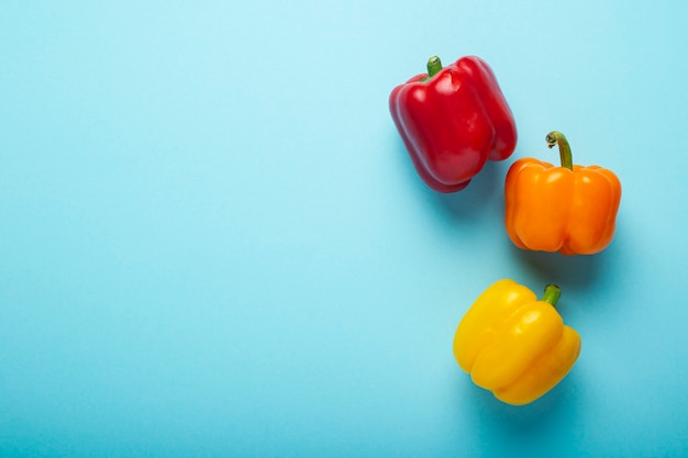 Drie verse heldere paprika's op een blauwe achtergrond. Bovenaanzicht, plat gelegd