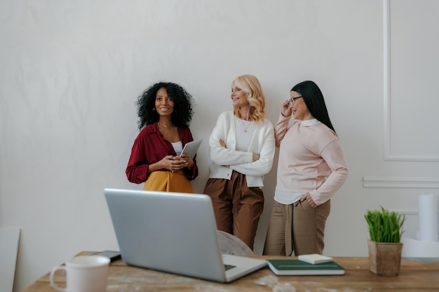 Drie volwassen vrouwen communiceren en glimlachen terwijl ze op de muur leunen in het kantoor