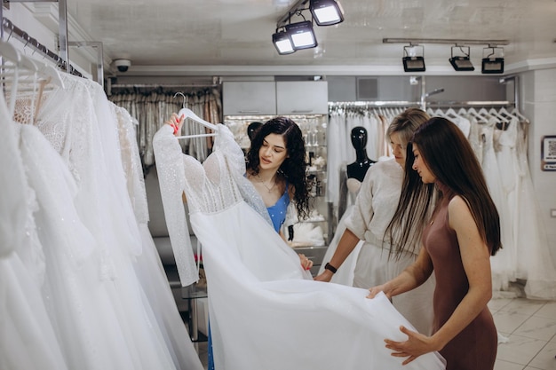 Drie vriendinnen A BrideToBe en bruidsmeisje die een trouwjurk proberen