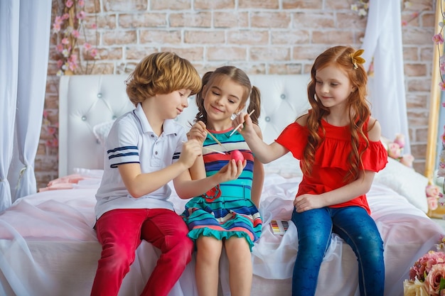 Drie vrolijke kinderen zitten samen en schilderen paasei. Happy Easter.Spring vakantie, traditie en mensen concept. Ijverige leerlingen die paasei schilderen.