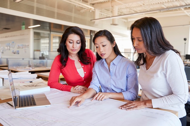 Drie vrouwelijke architecten die samen plannen bestuderen in een kantoor