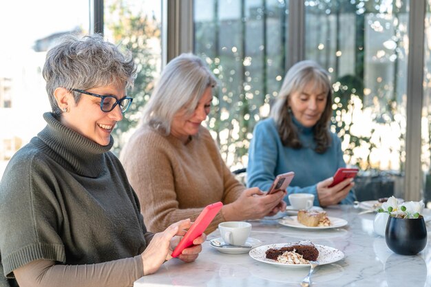 Foto drie vrouwelijke oudere vrienden met behulp van slimme telefoon en sociaal netwerk volwassen vrouwen technologie levensstijl cafetaria en ontbijt moment