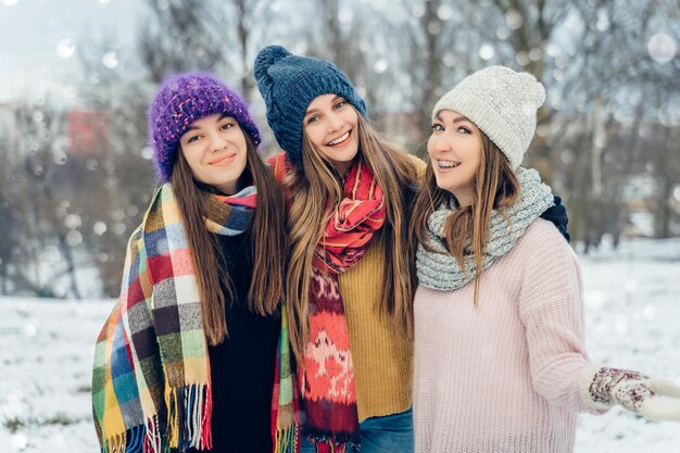 Foto drie vrouwelijke vrienden buiten in gebreide hoeden die plezier hebben op een sneeuwige koude weergroep van jonge vrouwtjes