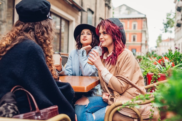 Drie vrouwelijke vrienden met drankjes in het buitencafé. Vrouwen kletsen en hangen samen tijdens de koffiepauze