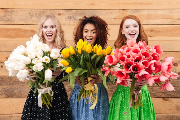 Foto drie vrouwen die boeketten van bloemen tonen bij camera