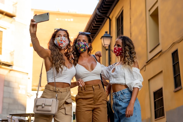 Drie vrouwen met maskers die mobiele celtelefoon met behulp van.