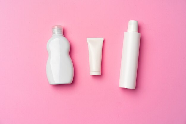 Drie witte cosmetische flessen op roze plat lag, bovenaanzicht