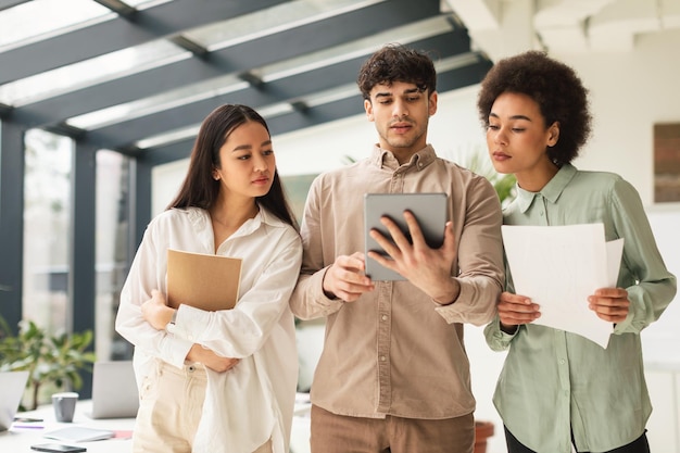 Drie zakelijke collega's die digitale tablet gebruiken die in een modern kantoor staan