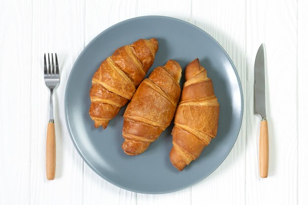 Drie zelfgemaakte gebakken croissants op plaat geserveerd met vork en mes bovenaanzicht