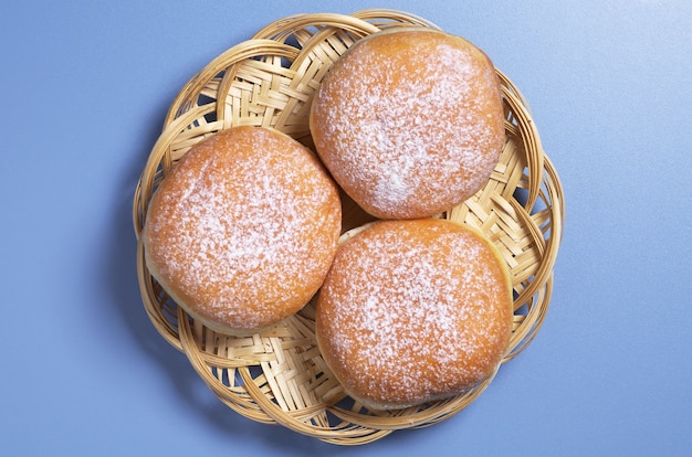 Foto drie zoete donuts in rieten plaat op blauwe tafel, bovenaanzicht