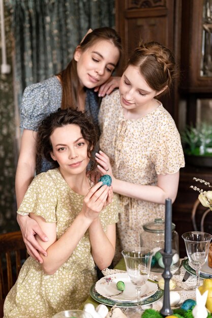 Drie zussen mooie jonge vrouwen klaar om de voorjaarsvakantie van vrolijk Pasen te vieren thuis eettafel met paaseieren in de hand te houden vintage platteland mode stijl van jurk