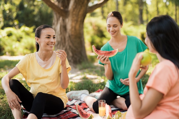 Drie zwangere vrouwen zitten in park op tapijt voor picknicks en eten