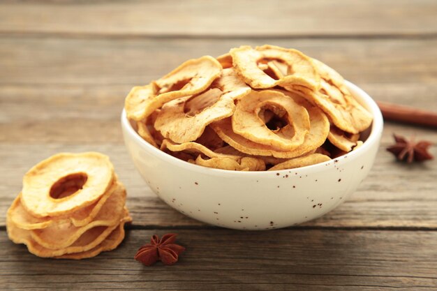 Dried apple chips in a bowl with fresh apple on grey wooden background