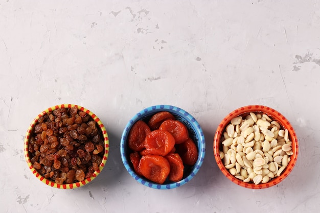 Dried apricot, raisins, peanuts in saucers, standing in a row on gray space. Top view. Space for text