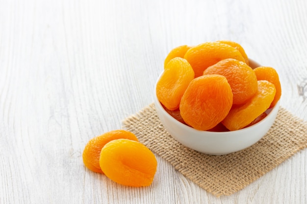 Dried apricots in a bowl on light wooden background.