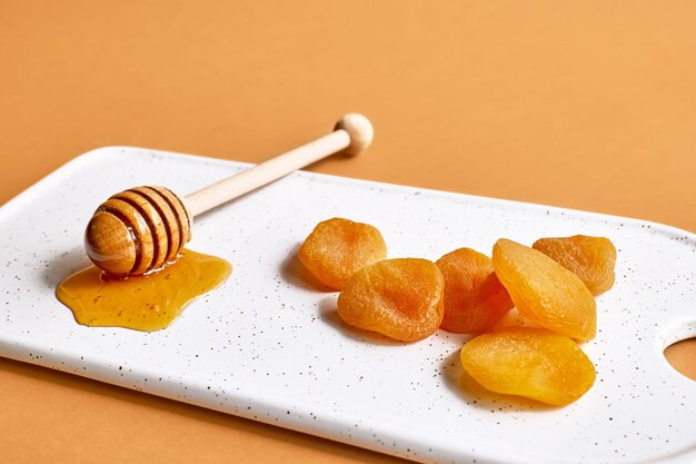 Dried apricots and honey in white plate on orange background