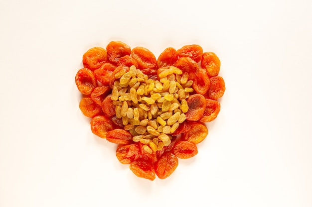 Dried apricots and raisins are laid out in the form of  hearts on a beige background